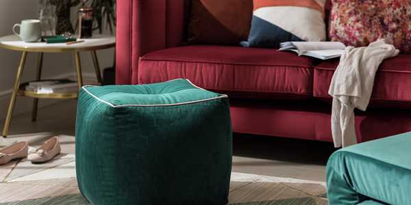 A velvet green pouffe in front of a sofa in a living room.